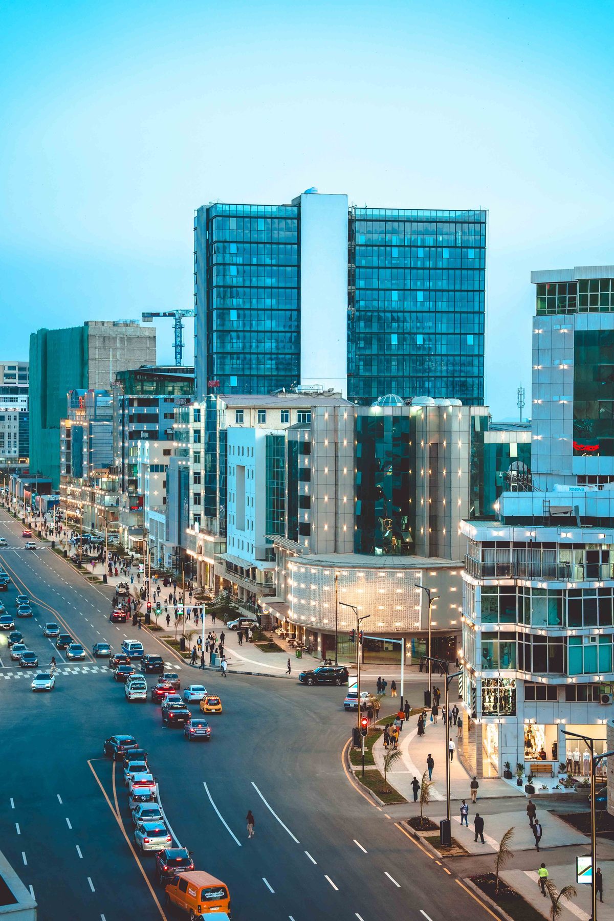 Bole Road in Addis Ababa at dusk, glass towers and lit shopfronts along a wide avenue with evening traffic and people crossing
