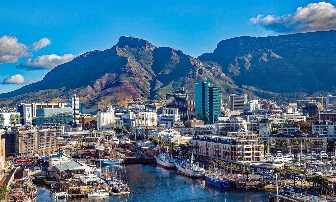 The V&A Waterfront in Cape Town at midday, yachts and quaysides in the foreground and Table Mountain and Devil's Peak rising directly behind the city centre