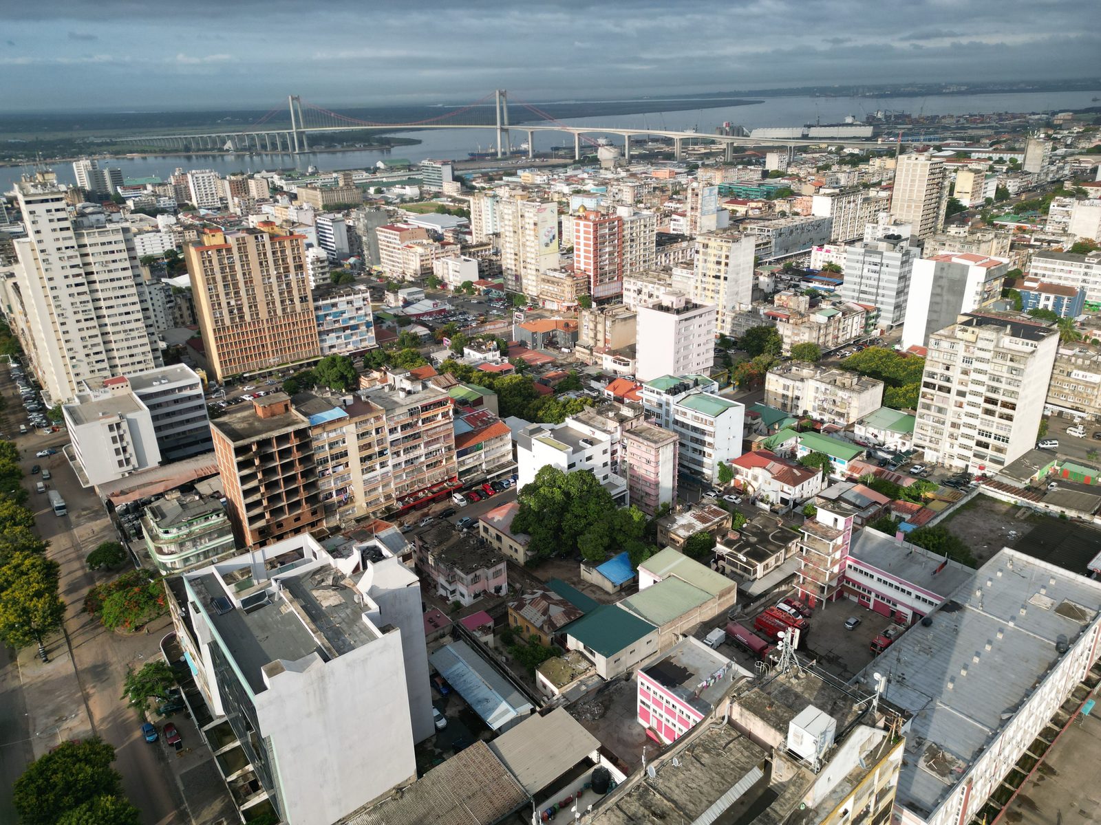 Maputo from the air: dense mid-rise blocks and tin roofs running down to the bay, ships at anchor, and the long span of the Maputo-Katembe bridge crossing the water in the distance
