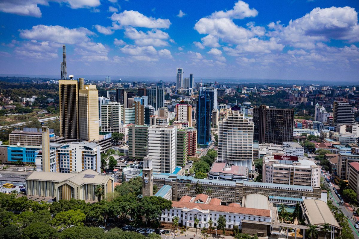 Central Nairobi from the air on a clear day, towers and older colonial-era rooftops in the foreground and the city spreading to the horizon under cumulus cloud