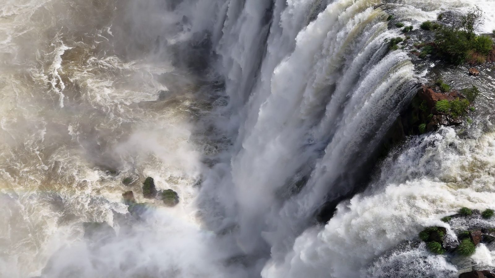 The lip of Victoria Falls in close-up, the river breaking white over the edge in full flood and spray rising back out of the gorge